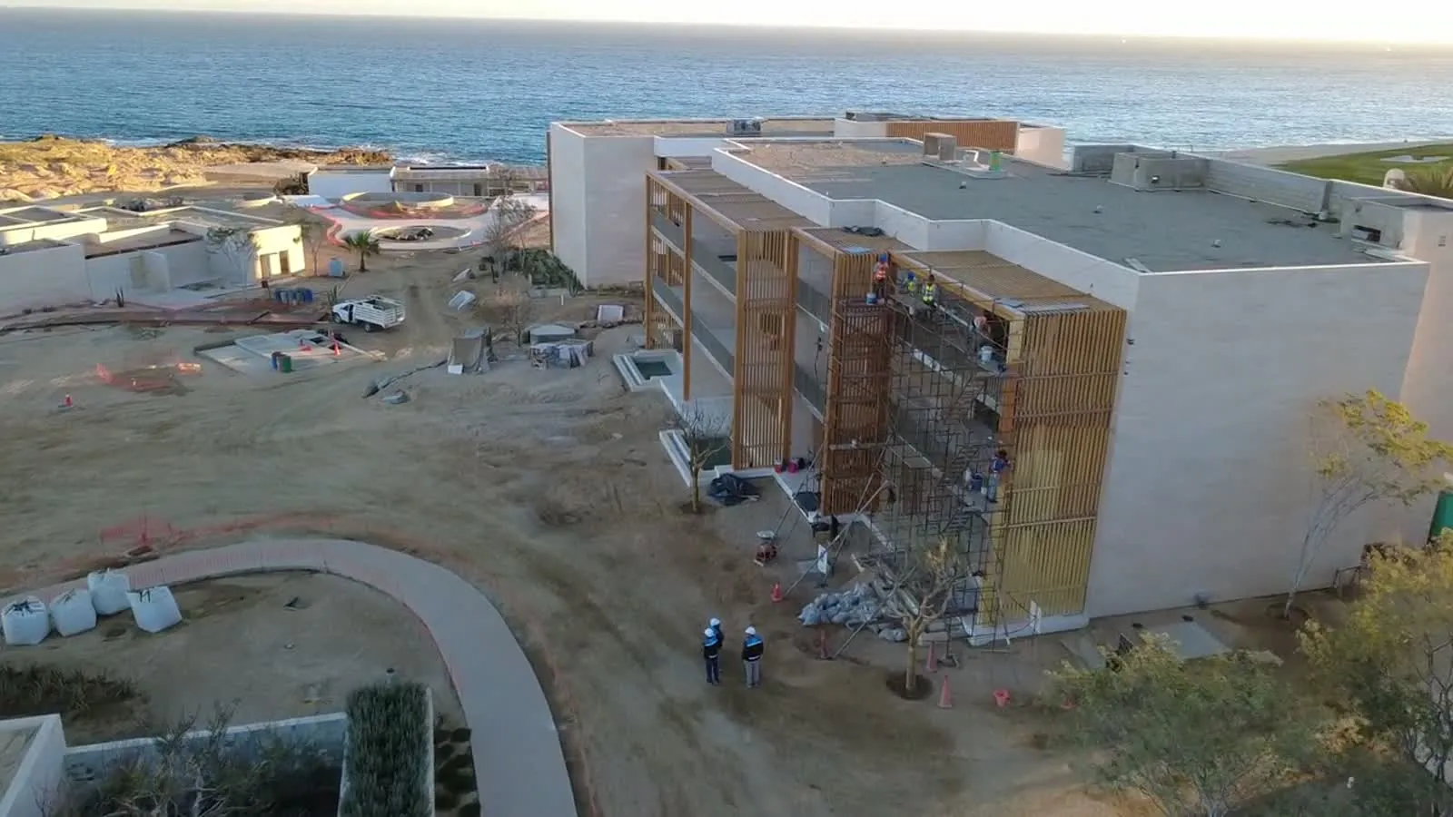 A three-storey building by the sea in fit-out, with timber screens and scaffolding, seen from a drone