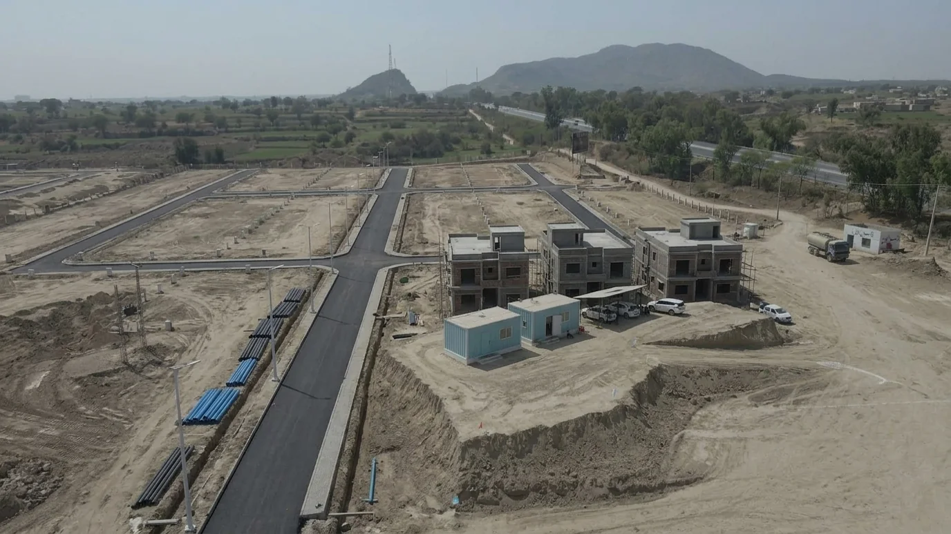 AI illustration: the same view a year later with asphalt roads, open trenches with water pipes and the first grey-structure houses