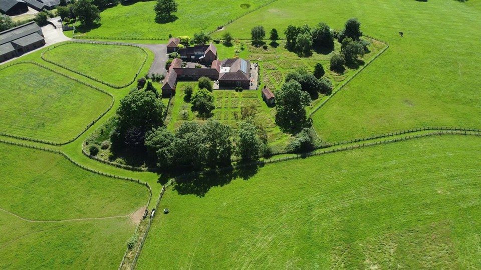Brick farmhouse and stables surrounded by fenced paddocks and woodland